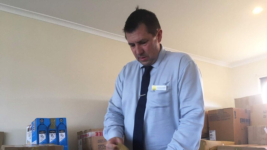 A man in a business shirt and tie tapes up a box in a room full of removal boxes.