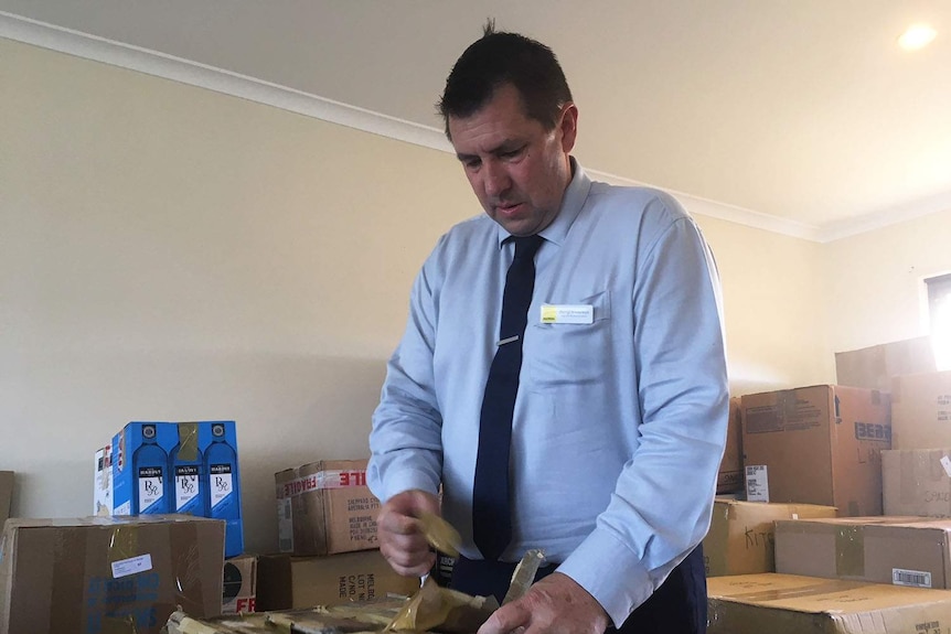A man in a business shirt and tie tapes up a box in a room full of removal boxes.