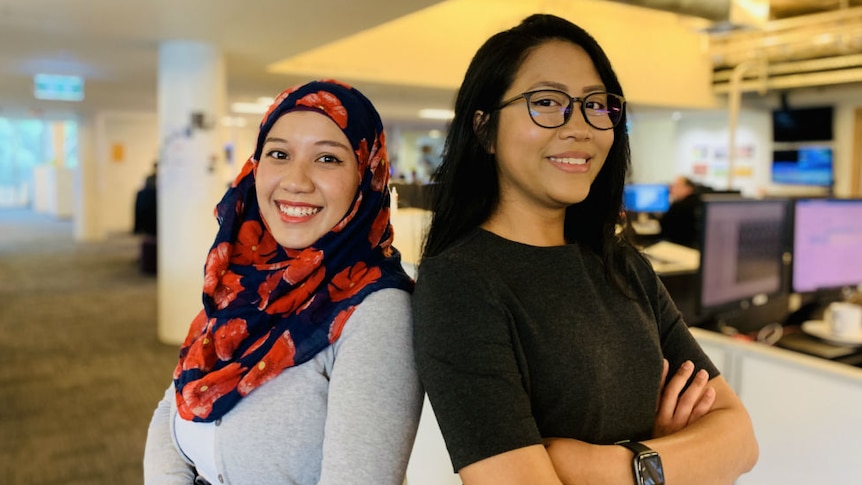 Azlan wearing headscarf and Jalal with backs against each other smiling at camera in newsroom.