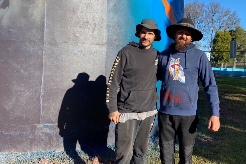 Two men stand together in front of heywood water tower