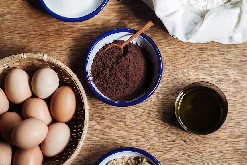Chocolate olive oil cake ingredients of cocoa powder, flour, eggs, sugar and olive oil on a wood table
