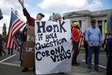 A protester holding a sign reading "Honk if you question coronavirus"