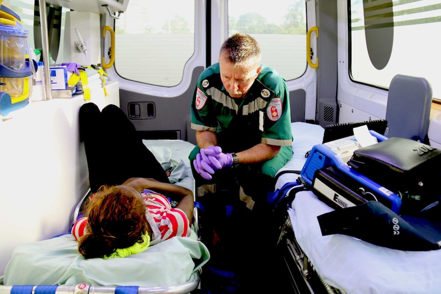 A male paramedic sits beside a female patient in the  back of an ambulance