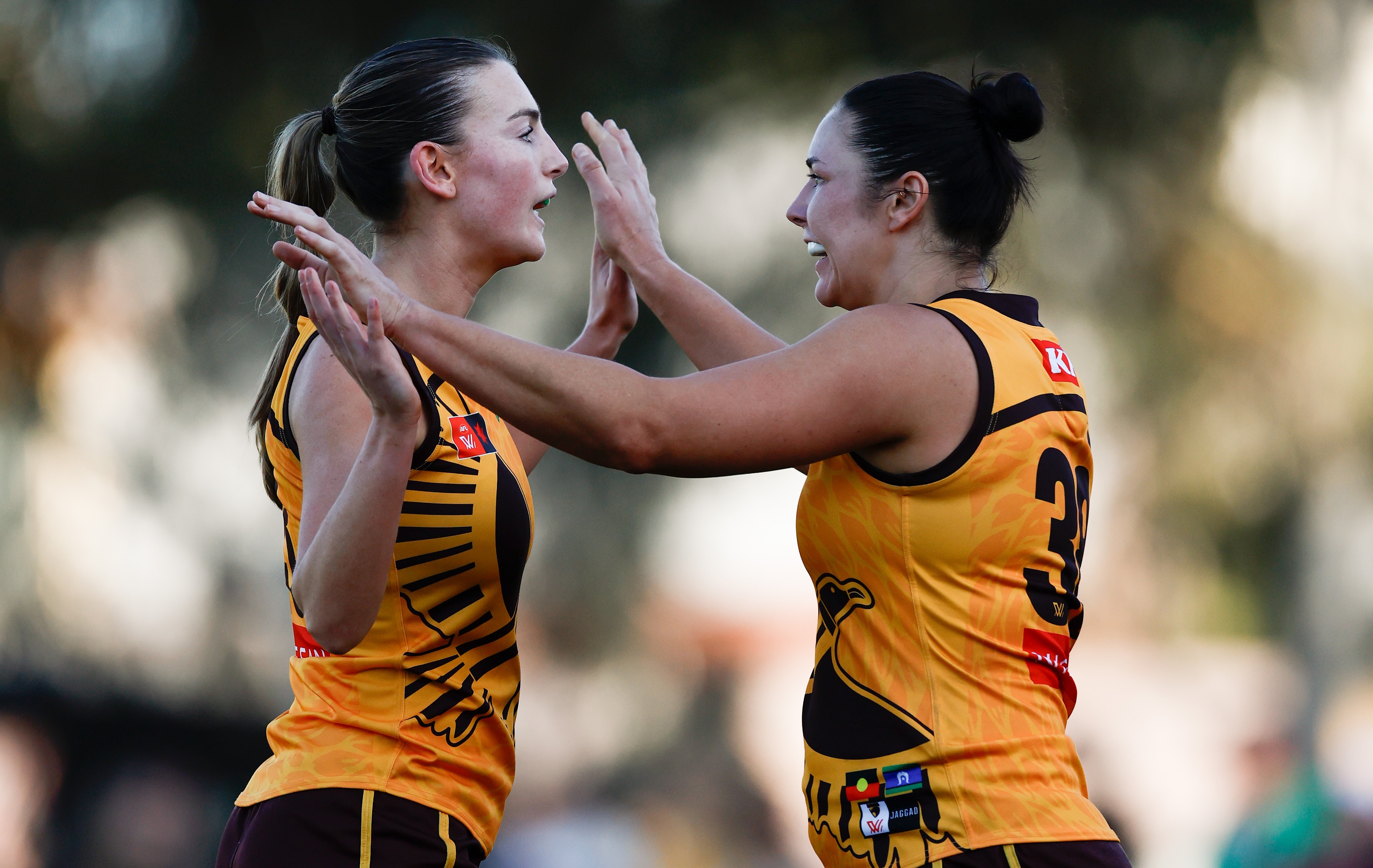 Two Hawthorn AFLW players clasp hands in celebration after a goal.