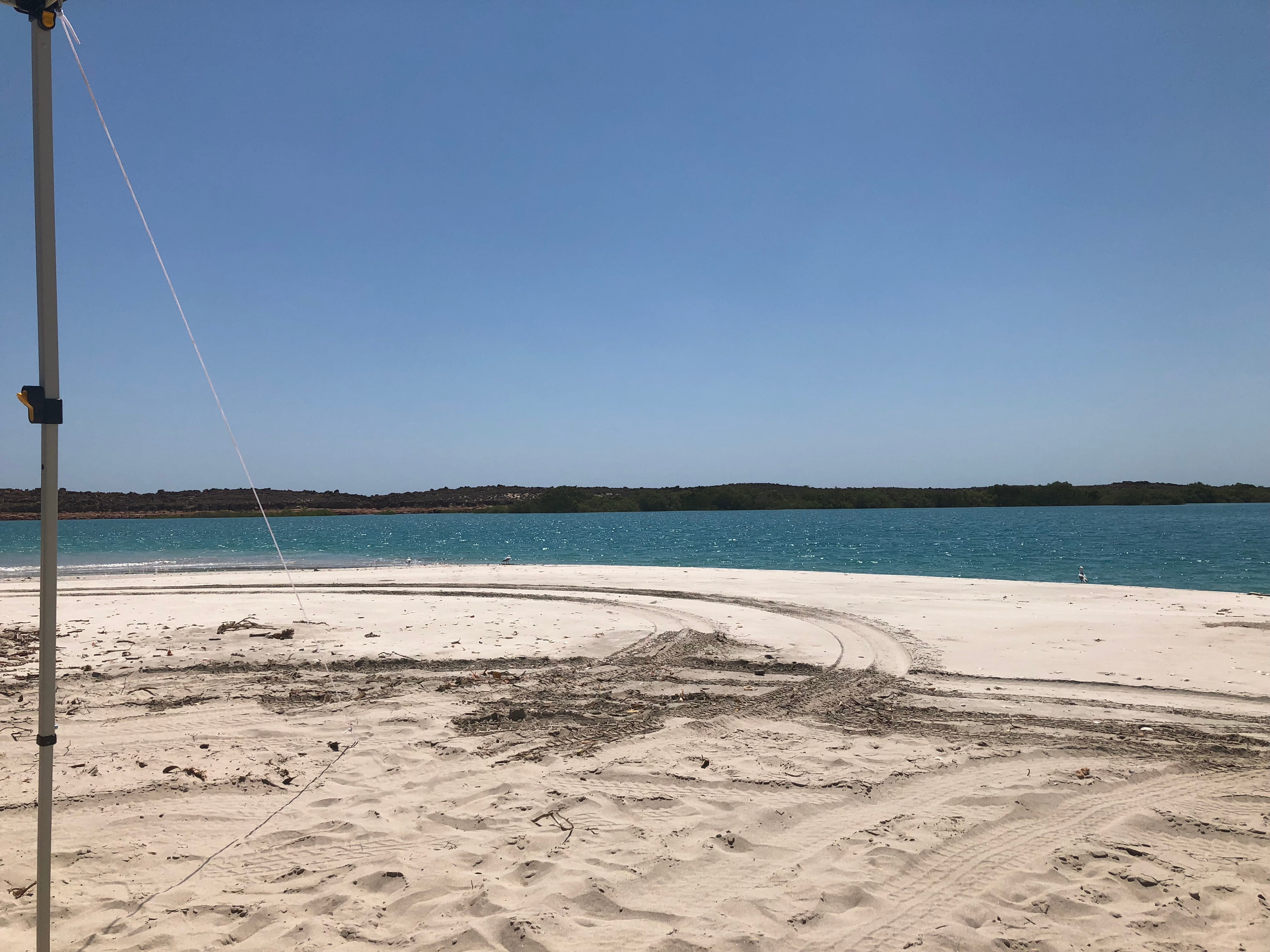 White sandy beach with blue water and rocks in background.