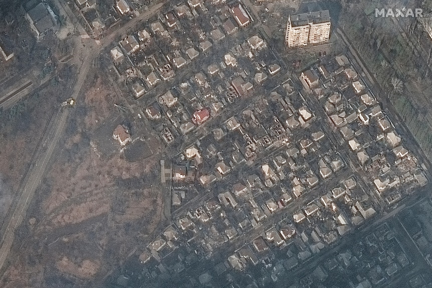 A satellite image shows a top-down view of damaged houses, buildings, roads, trees and parklands.