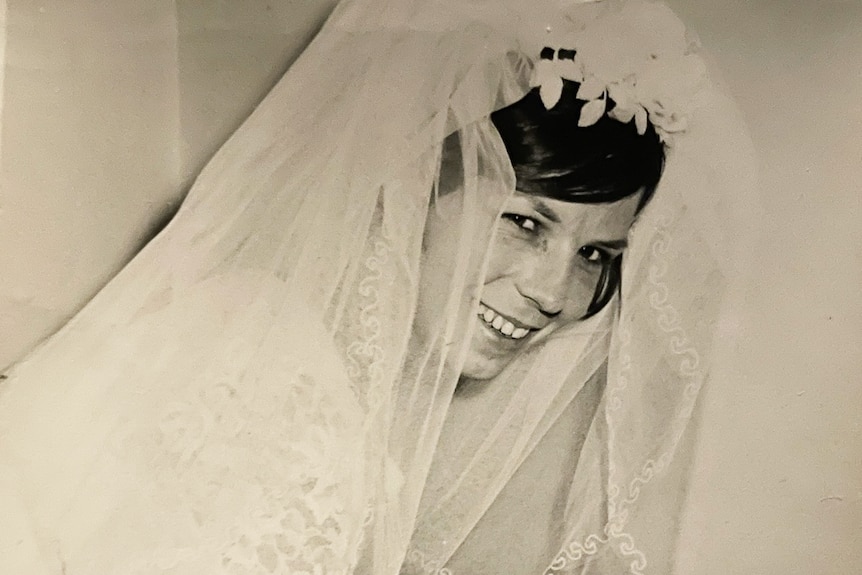 An old black and white photo of a young woman in bridal wear smiling at the camera