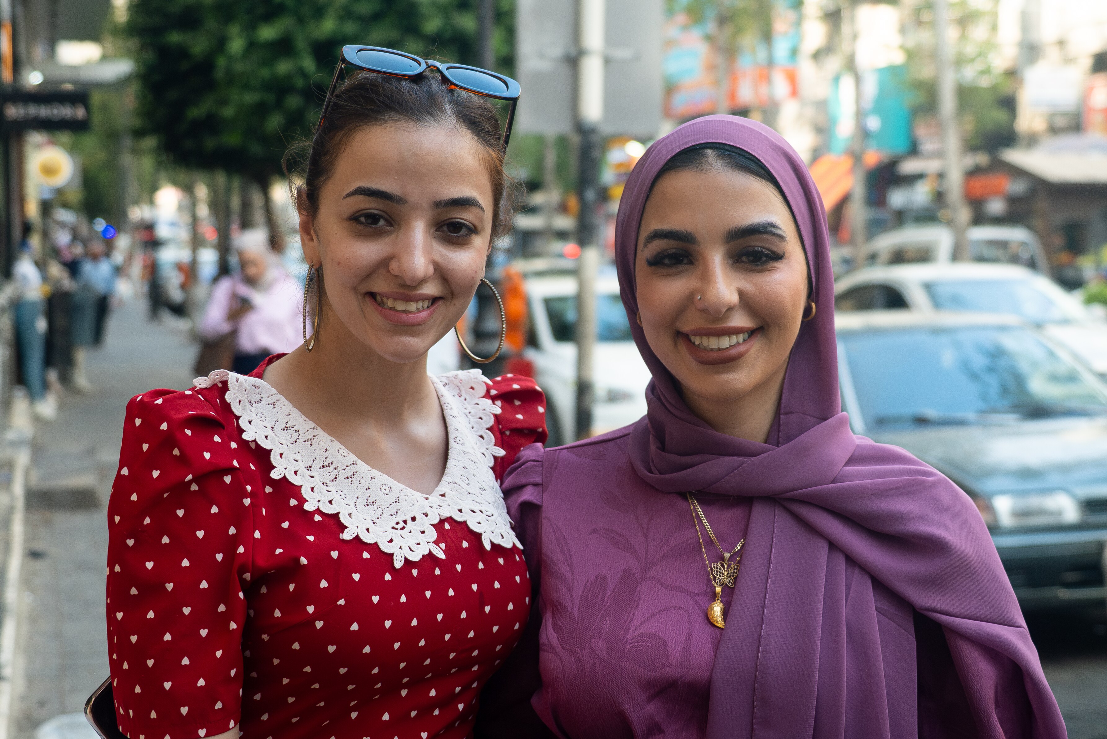 two women, one in a purple head dress and the other in a red dress speak to a camera