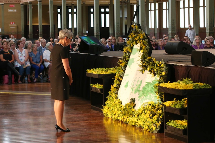 Linda Dessau pauses before a floral map of Victoria at a bushfire commemoration ceremony.