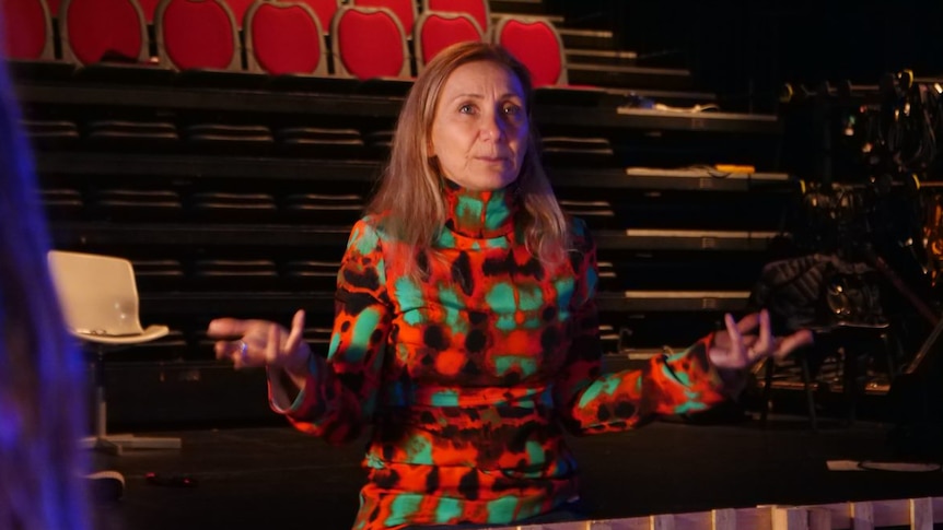 Deborah Leiser-Moore holds her hands out as she stands in front of the audience seats inside the theatre.