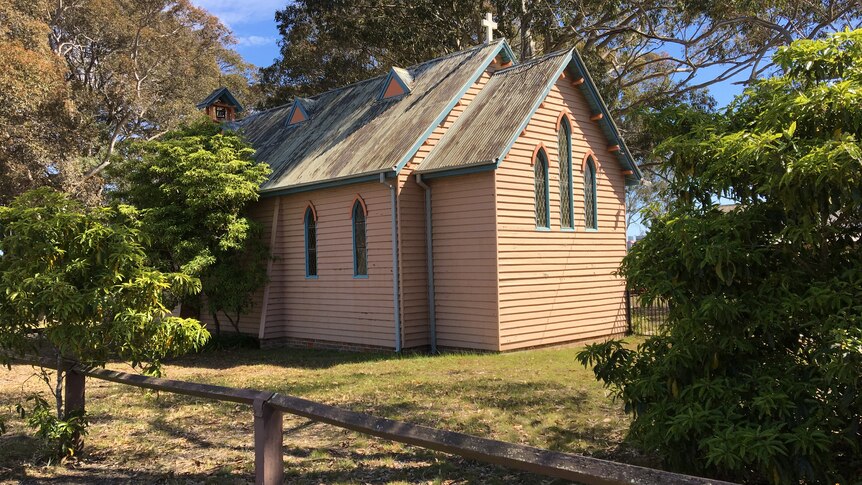 An old timber weatherboard church surrounded by trees.