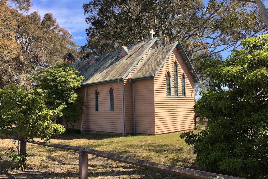 An old timber weatherboard church surrounded by trees.