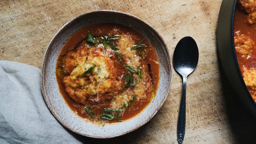 A bowl of smoky tomato soup with spring onion dumplings and melted cheese, a comforting one-pot recipe.