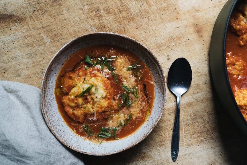 A bowl of smoky tomato soup with spring onion dumplings and melted cheese, a comforting one-pot recipe.