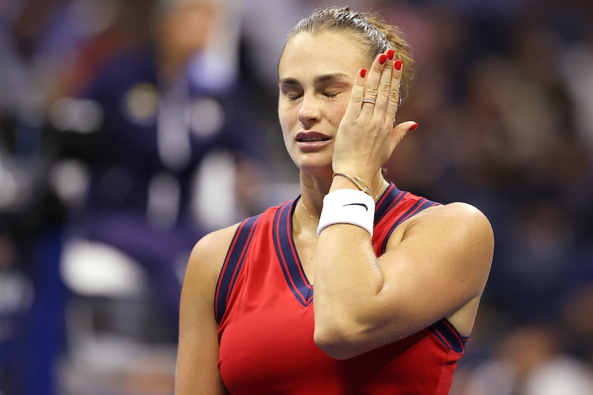 A female tennis player closes her eyes in frustration and puts her hand to the side of her face during a match.
