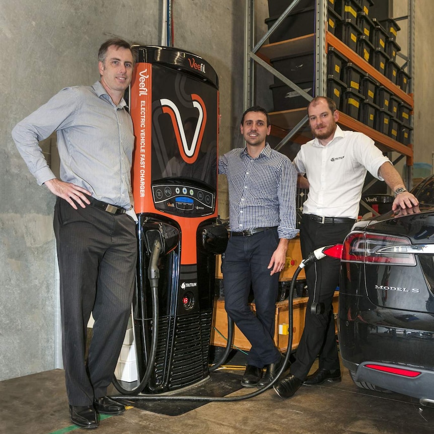 Three men with a six-foot tall EV charger
