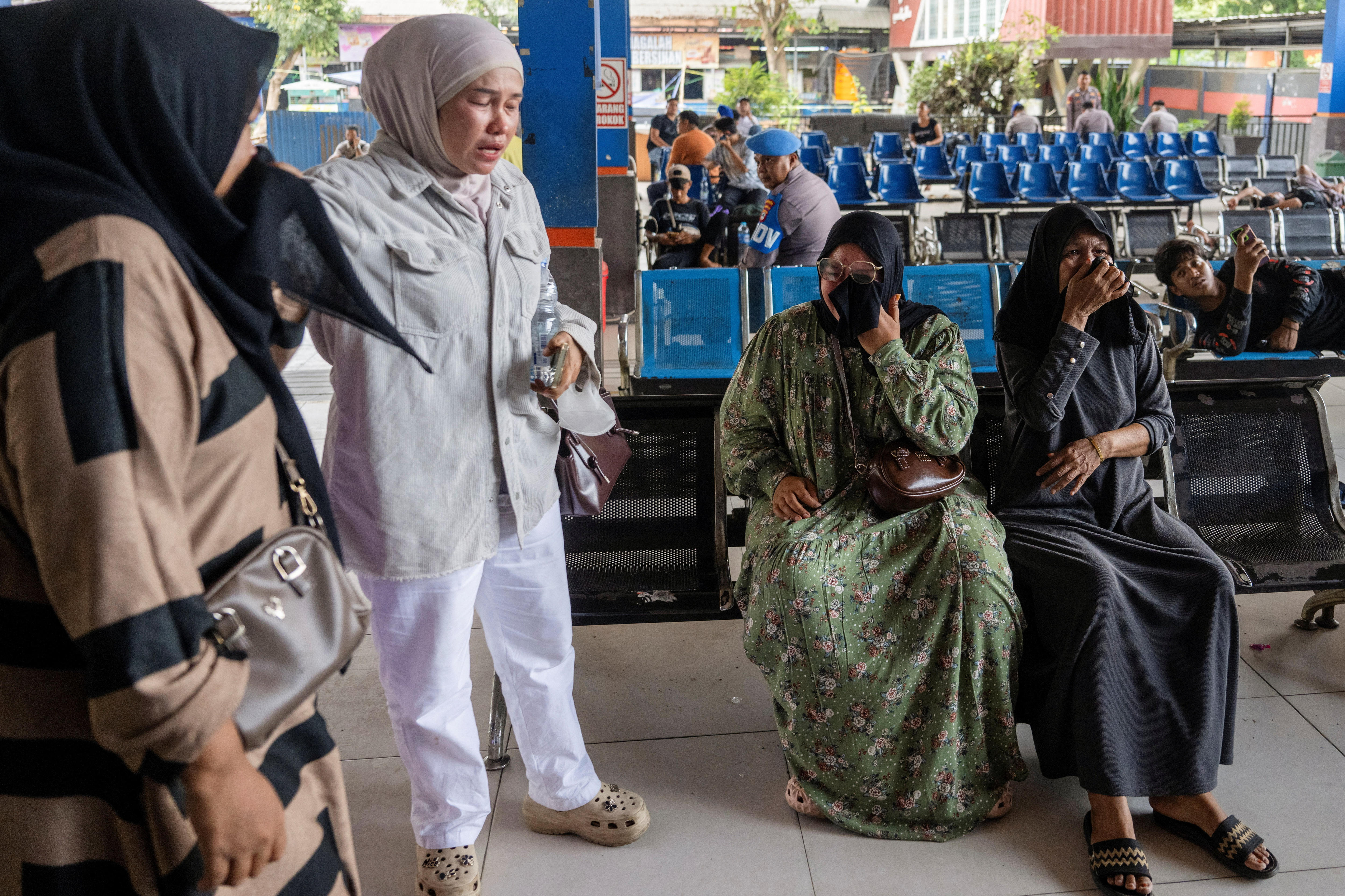 Three women cry while seated at a ferry terminal