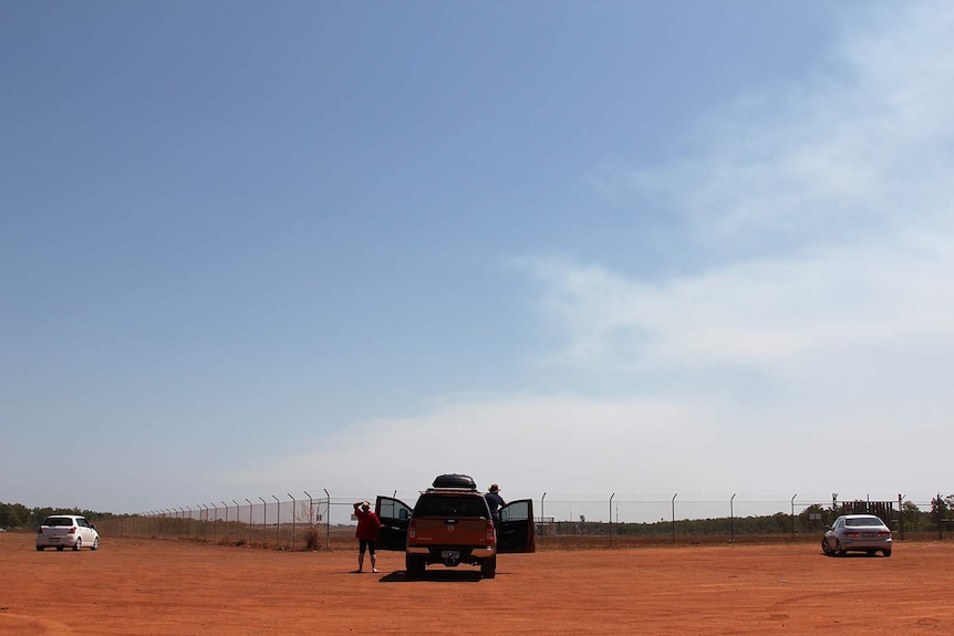 A group of three cars pulled up at the fence of the Darwin airport, with one couple looking towards the skies.
