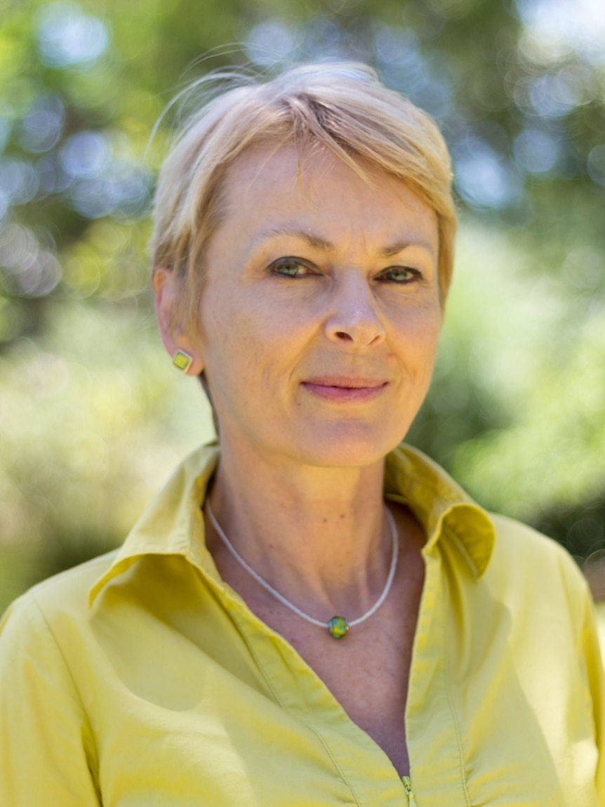 A blonde woman with short hair in a yellow shirt smiles at thew camera.