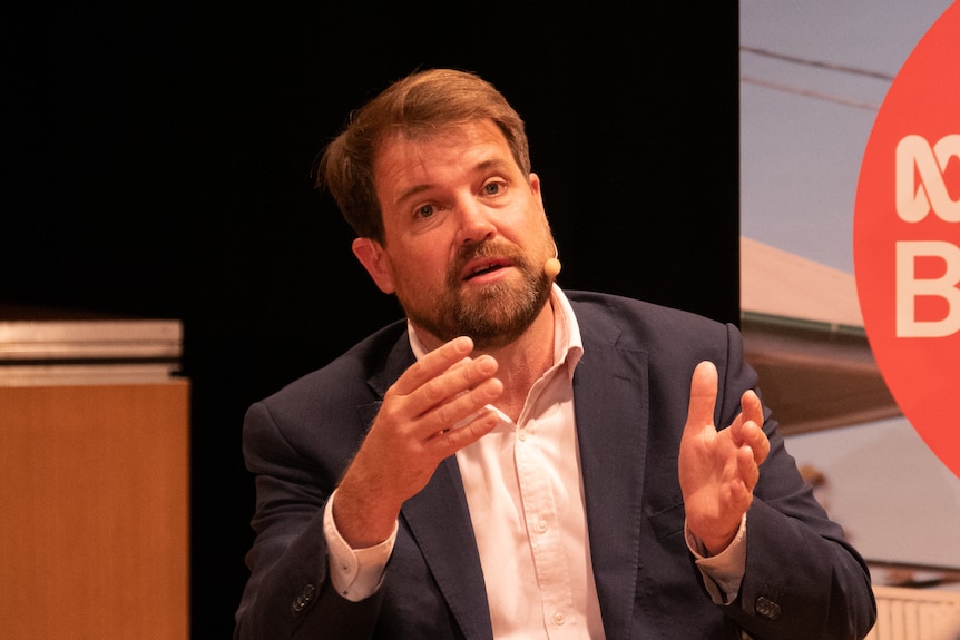 A bearded man in an open-neck business shirt and dark blazer speaks at a forum held by ABC Radio Brisbane