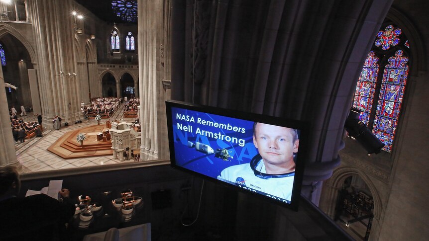 A screen shows an image of Neil Armstrong during a memorial service at the National Cathedral in Washington DC.