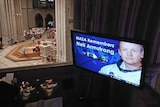 A screen shows an image of Neil Armstrong during a memorial service at the National Cathedral in Washington DC.