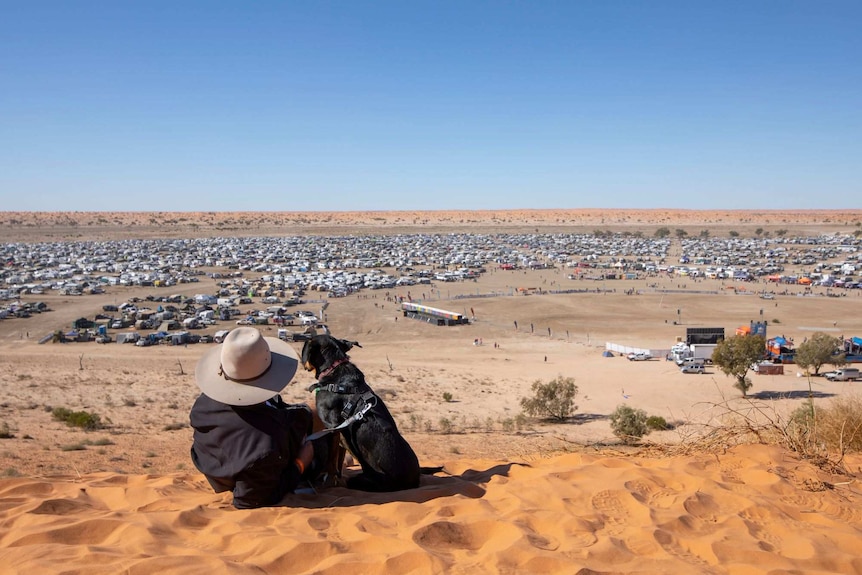 Birdsville's Big Red Bash collection of caravans viewed by a child from a sand dune in the Simpson Desert