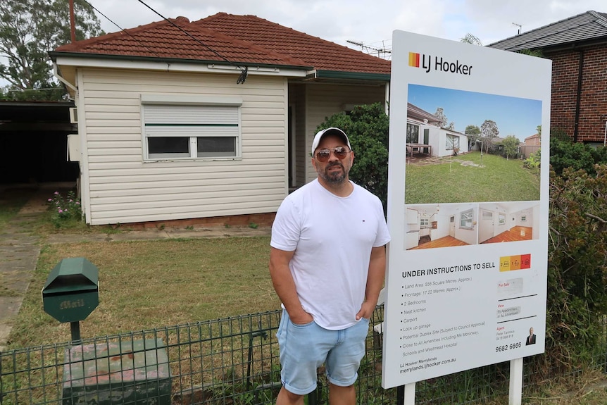 Haig Abraham standing next to a 'for sale' sign outside a house he is trying to sell.