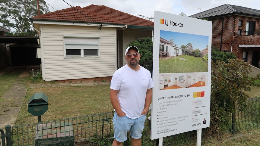 Haig Abraham standing next to a 'for sale' sign outside a house he is trying to sell.