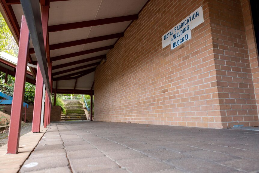 A brick wall and a tin awning and concrete path at a school campus 