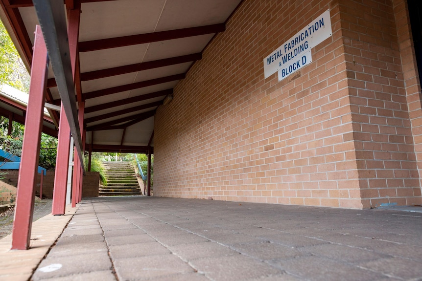 A brick wall and a tin awning and concrete path at a school campus 