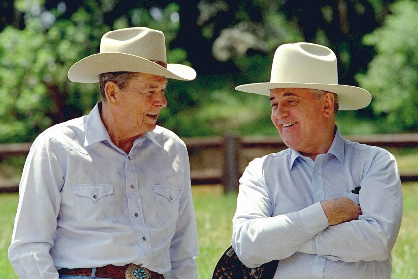 Ronald Reagan and Mikhail Gorbachev in cowboy hats leaning against a fence 