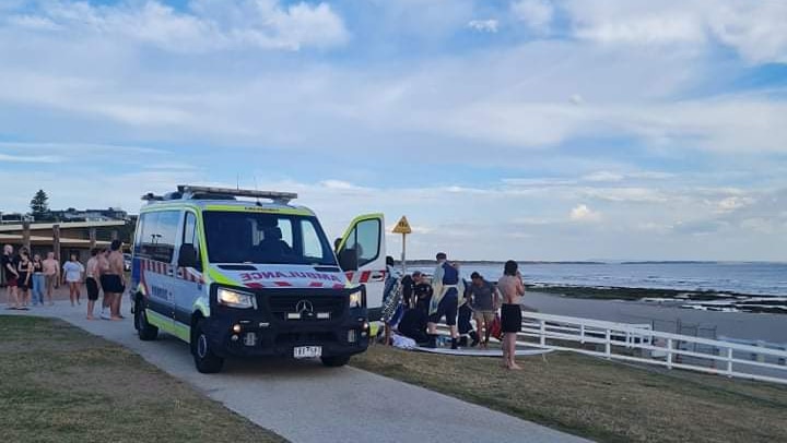 People crowd around an ambulance on a beachside road