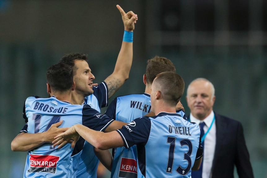 Bobo raises his left arm to the crowd as he is hugged by his Sydney FC teammates against Wellington Phoenix.