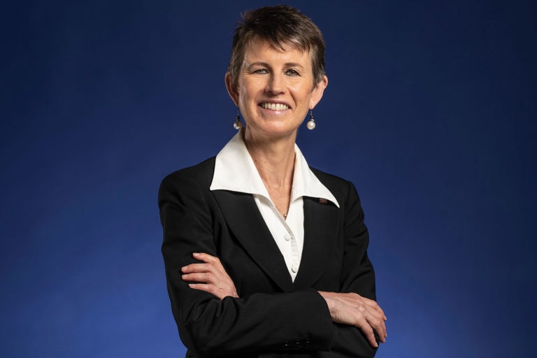 A woman stands smiling for a professional portrait photograph.