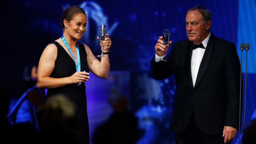 John Newcombe and Ash Barty raise glasses of champagne on stage after Barty wins Tennis Australia's Newcombe Medal.