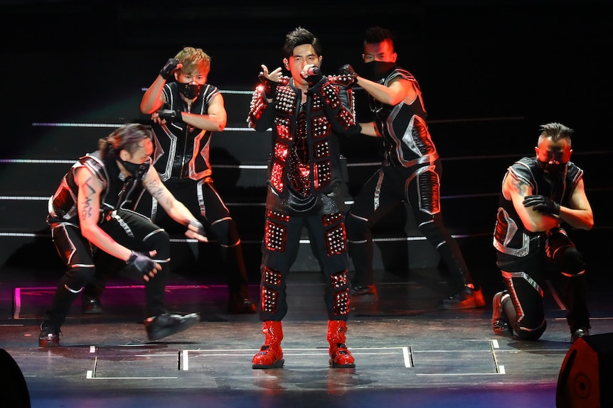 Jay Chou in black performing on stage with another four dancers. 