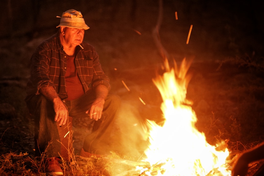 Indigenous man sitting next to a camp fire.