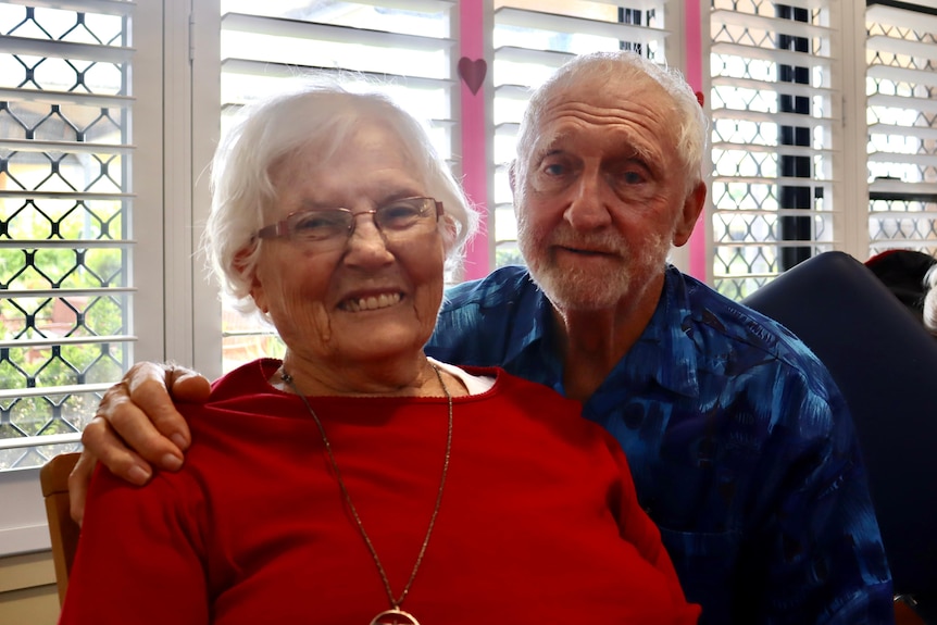 Elderley man and woman smile at camera with Valentine's Day decorations in the background