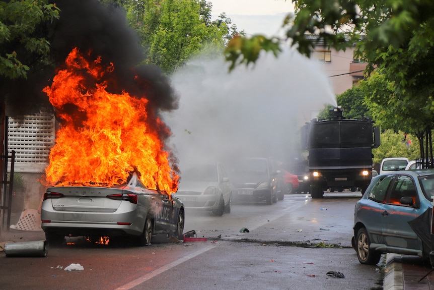 A police water cannon tries to extinguish the fire from a burning police car.