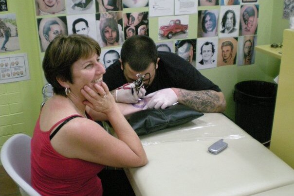 A woman sits while a man tattoos her forearm.  For a story on getting a memorial tattoo after the loss of a son. 