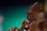Profile view of Jacob Zuma, sitting expressionless with hands clasped in front of him.