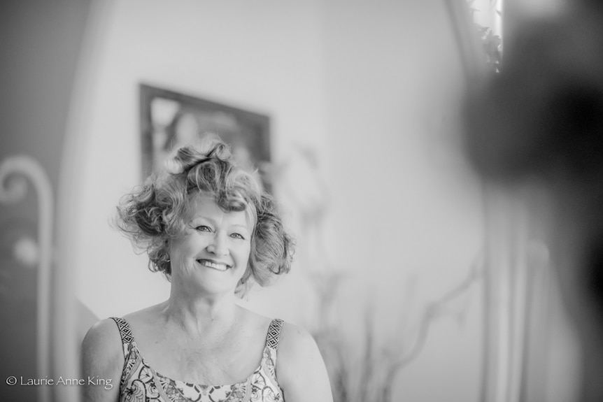 Lady with curlers in her hair smiling into the reflection of the mirror