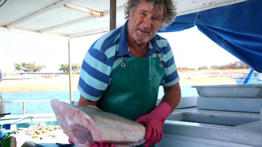 A man holding a piece of shark meat on a boat