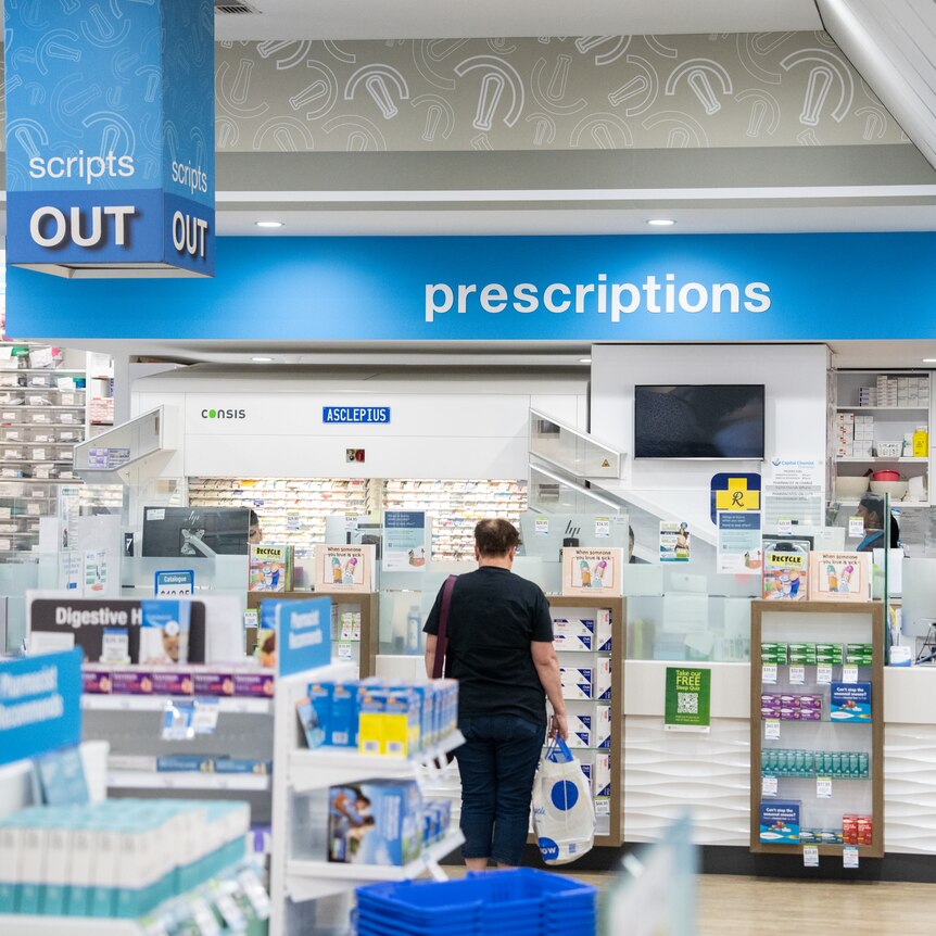 A script counter at a pharmacy, with a man waiting in line.