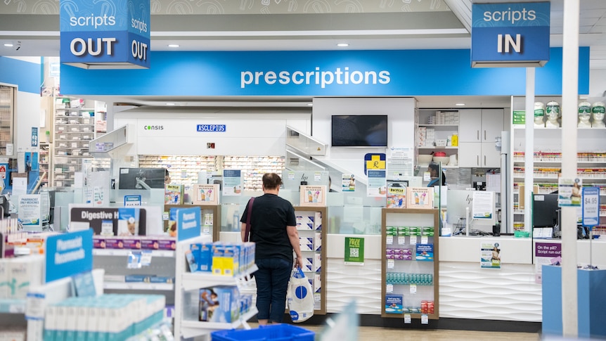 A script counter at a pharmacy, with an unidentifiable man waiting in line.