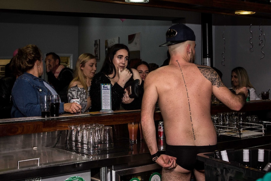 A male barman wearing only underwear is pictured from behind.