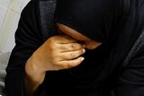 A woman wearing a black hijab weeping into her hand. 