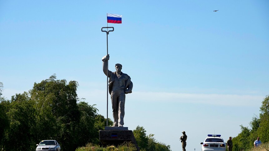 A Russian soldier stands in the road at the entrance of Mariupol with a Soviet style symbolic monument of a metallurgist. 