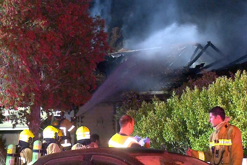 firefighters spraying down a smouldering and charred house